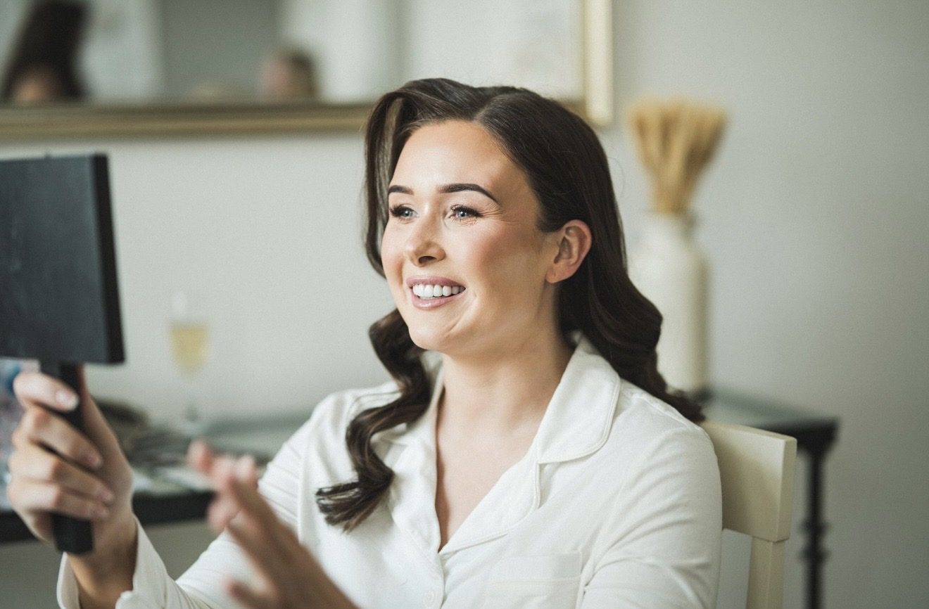 Bride smiling as she sees her finished makeup in a mirror
